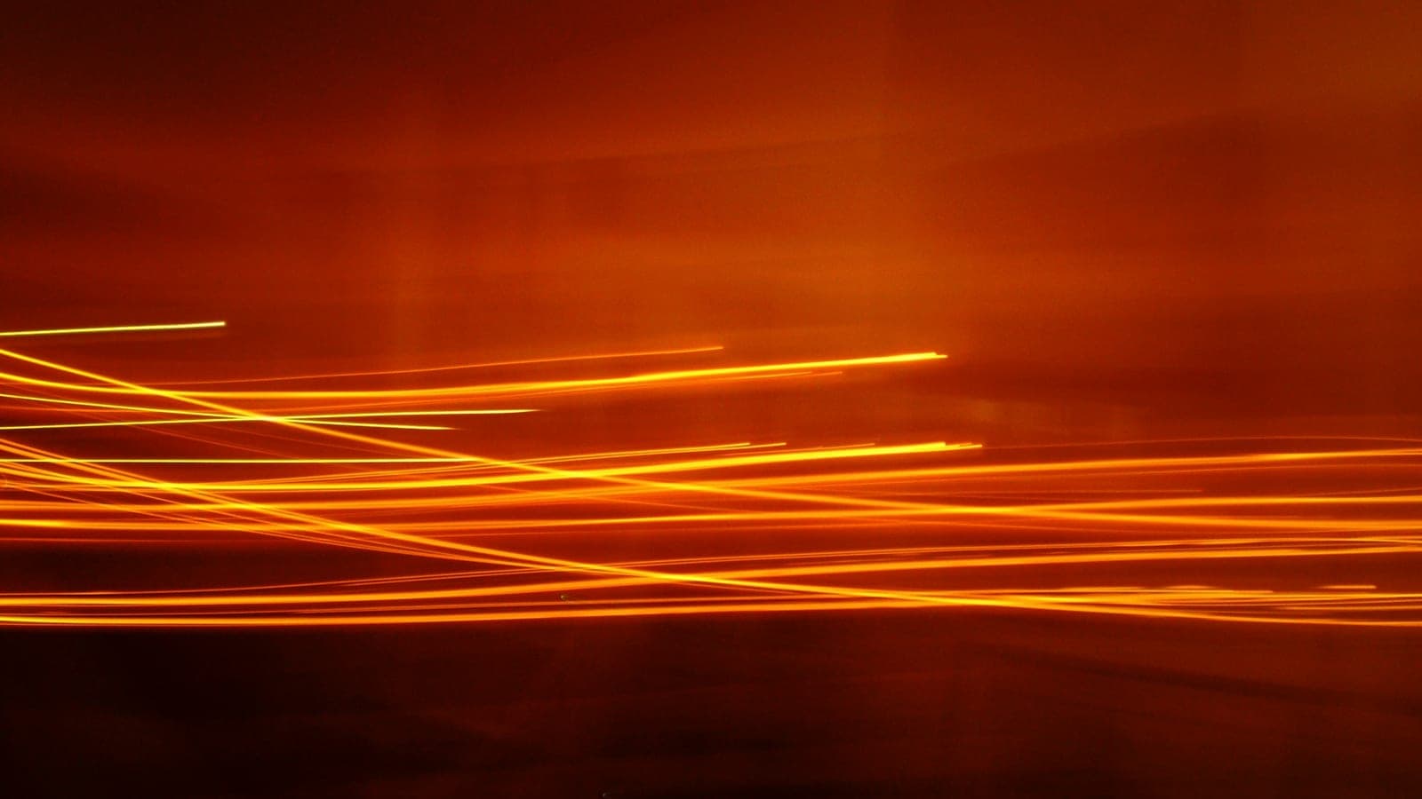 Long-exposure orange light streaks racing across a dark ground, the paths of motion recorded as trails