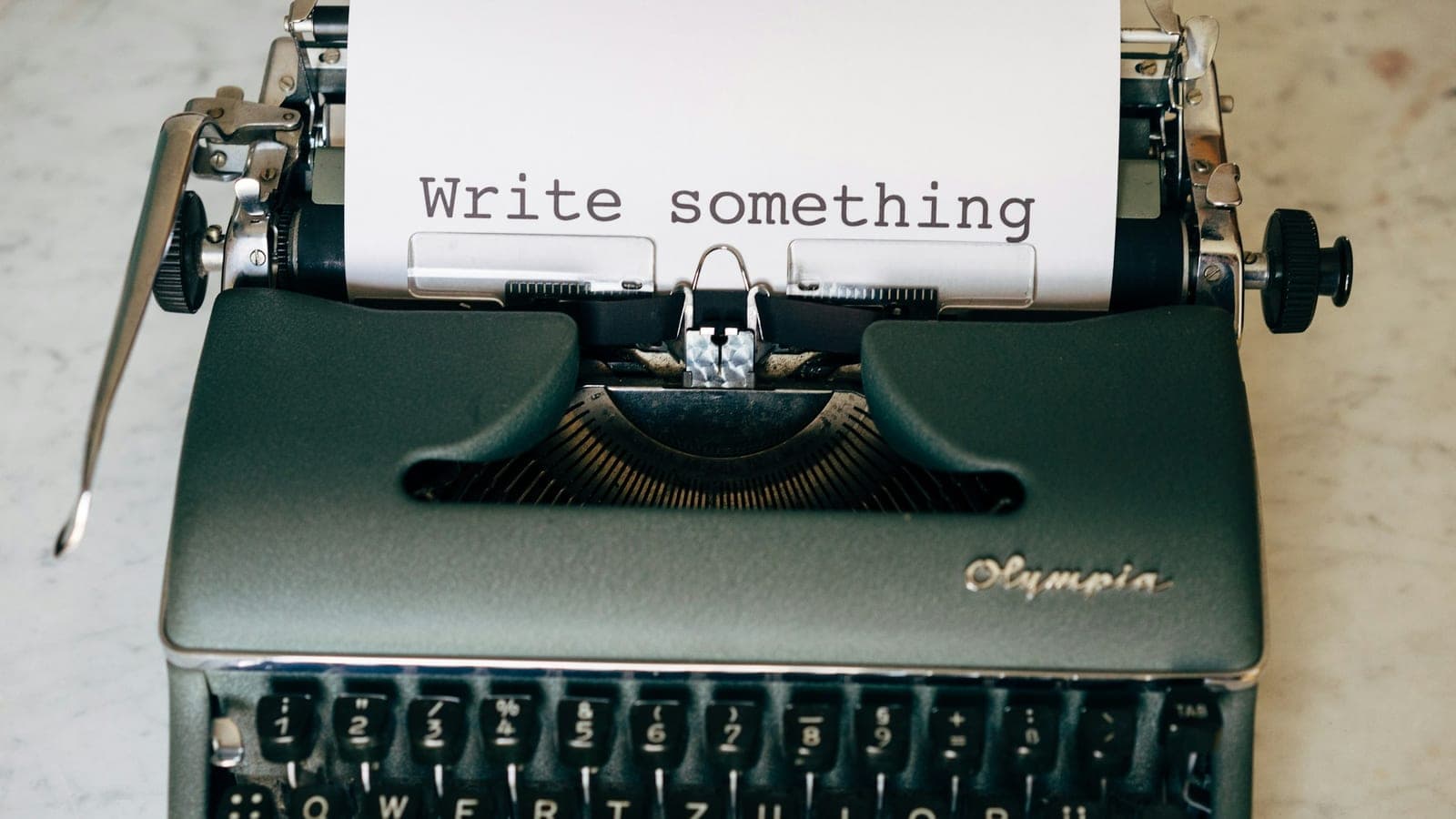 An Olympia typewriter on a marble surface, a sheet in the platen reading "Write something"