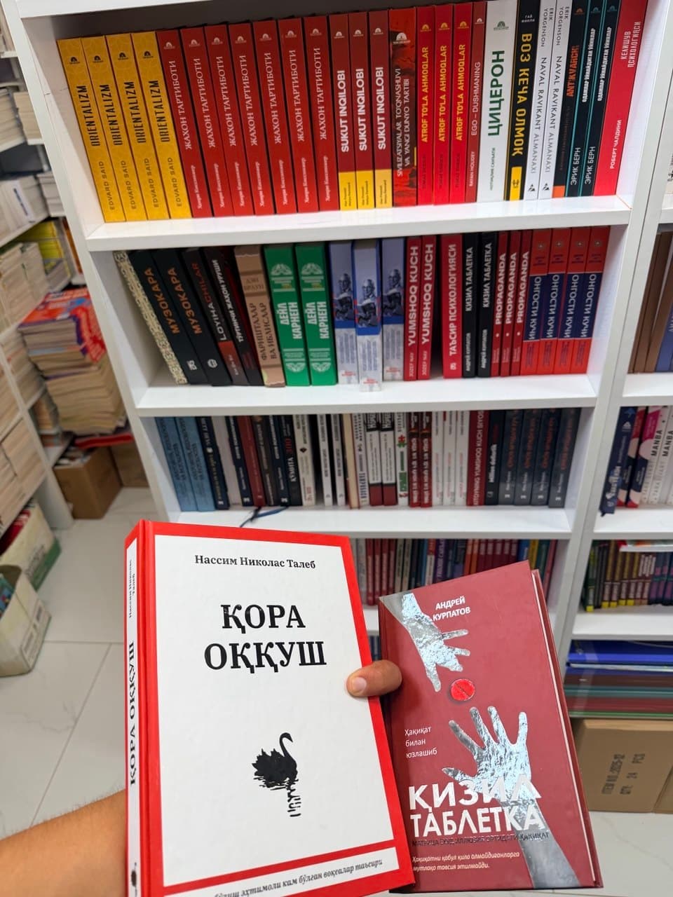 Holding Uzbek editions of Nassim Taleb's The Black Swan and Andrey Kurpatov's Red Pill in front of a bookshop shelf